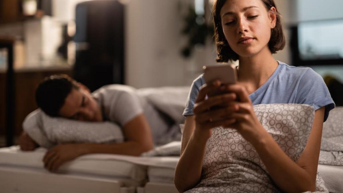 Mujer mira móvil mientras marido duerme