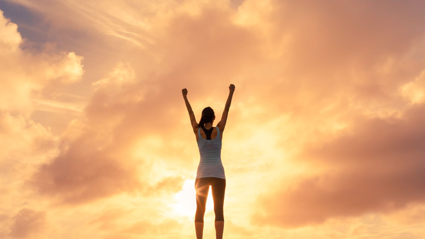 Una mujer levanta los brazos mirando al sol
